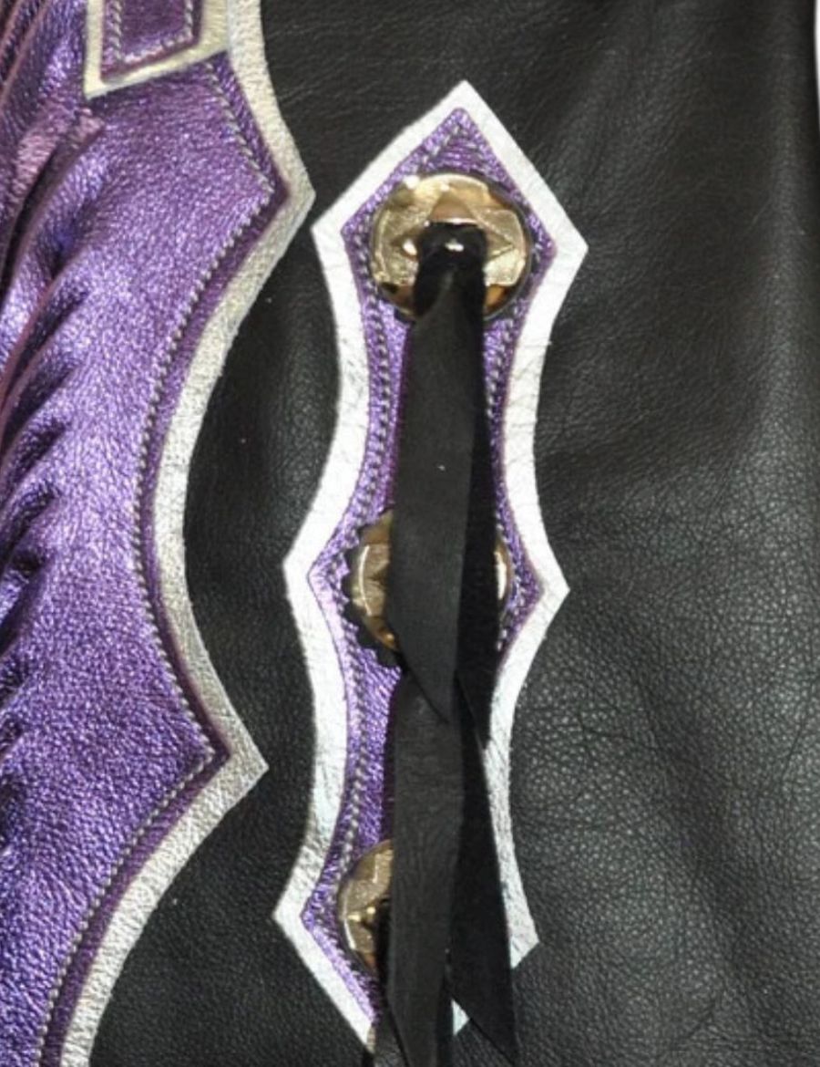 Close-up of American flag rodeo chaps featuring silver conchos, black leather ties, and metallic purple trim accents.
