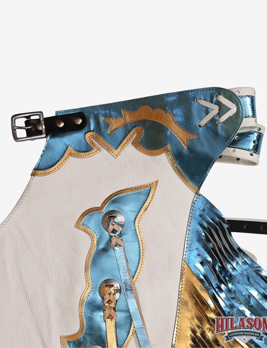 Close-up yoke view of white rodeo chaps featuring metallic blue leather overlays and western buckle detailing.