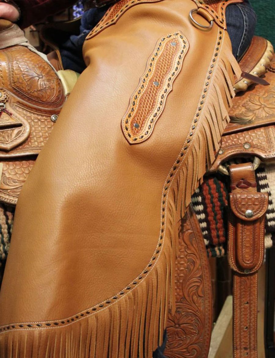 Angled close view of basketweave cowhide chinks chaps showing fringe detail and premium western leatherwork.