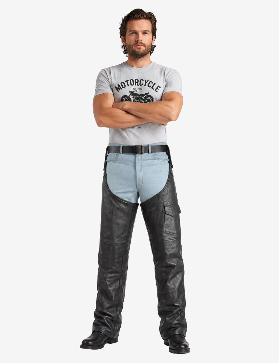 Full model wearing biker assless chaps with removable belt in black genuine leather with relaxed motorcycle fit and utility pocket.