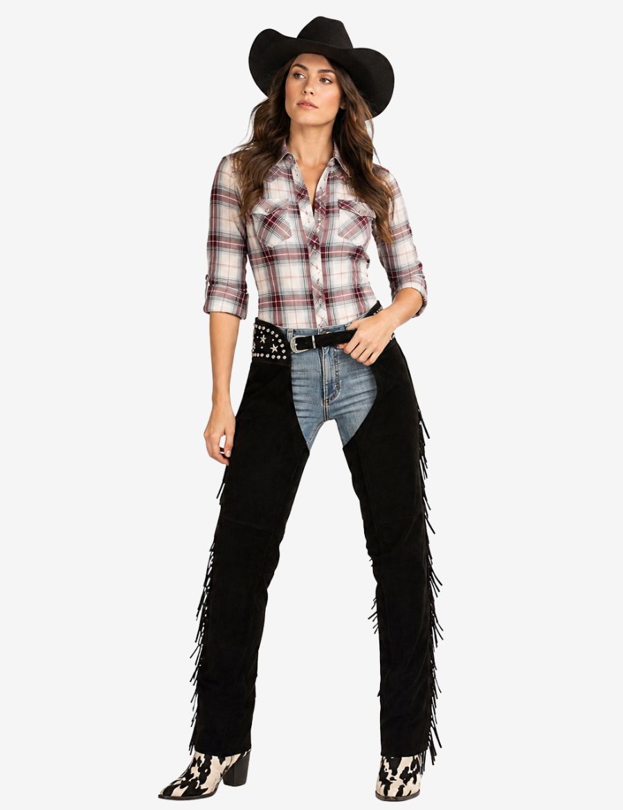 Woman wearing black cowgirl assless chaps with fringe, plaid western shirt, cowboy hat, and boots.