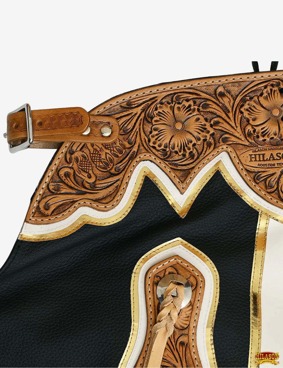 Close-up tooling detail of black rodeo chaps featuring floral carved leather and braided tassels.