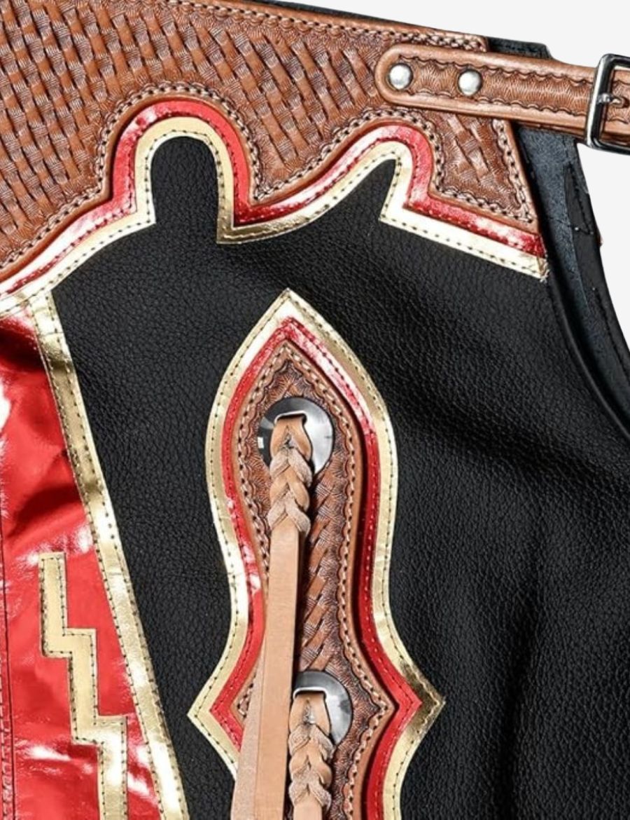 Close-up yoke view of black leather rodeo chaps with metallic red fringe and detailed western tooling accents.