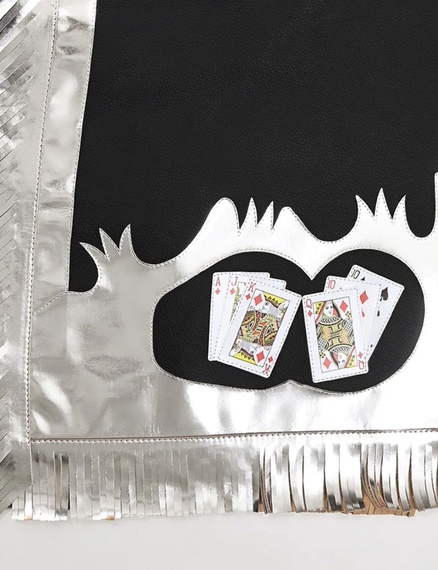 Close-up of black and silver bull riding chaps showing playing card artwork, silver trim, and western fringe accents.