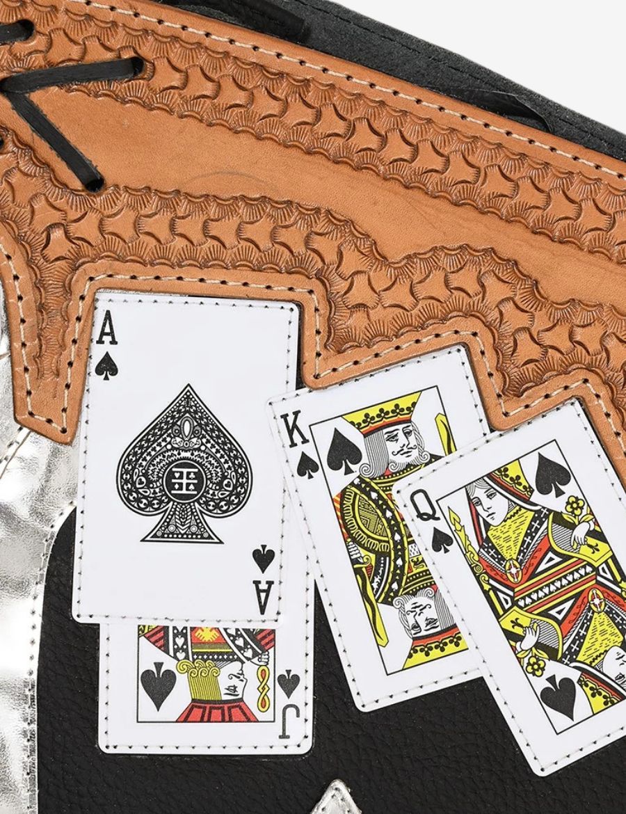 Detailed view of black and silver bull riding chaps with hand tooled leather yoke and poker card western artwork.
