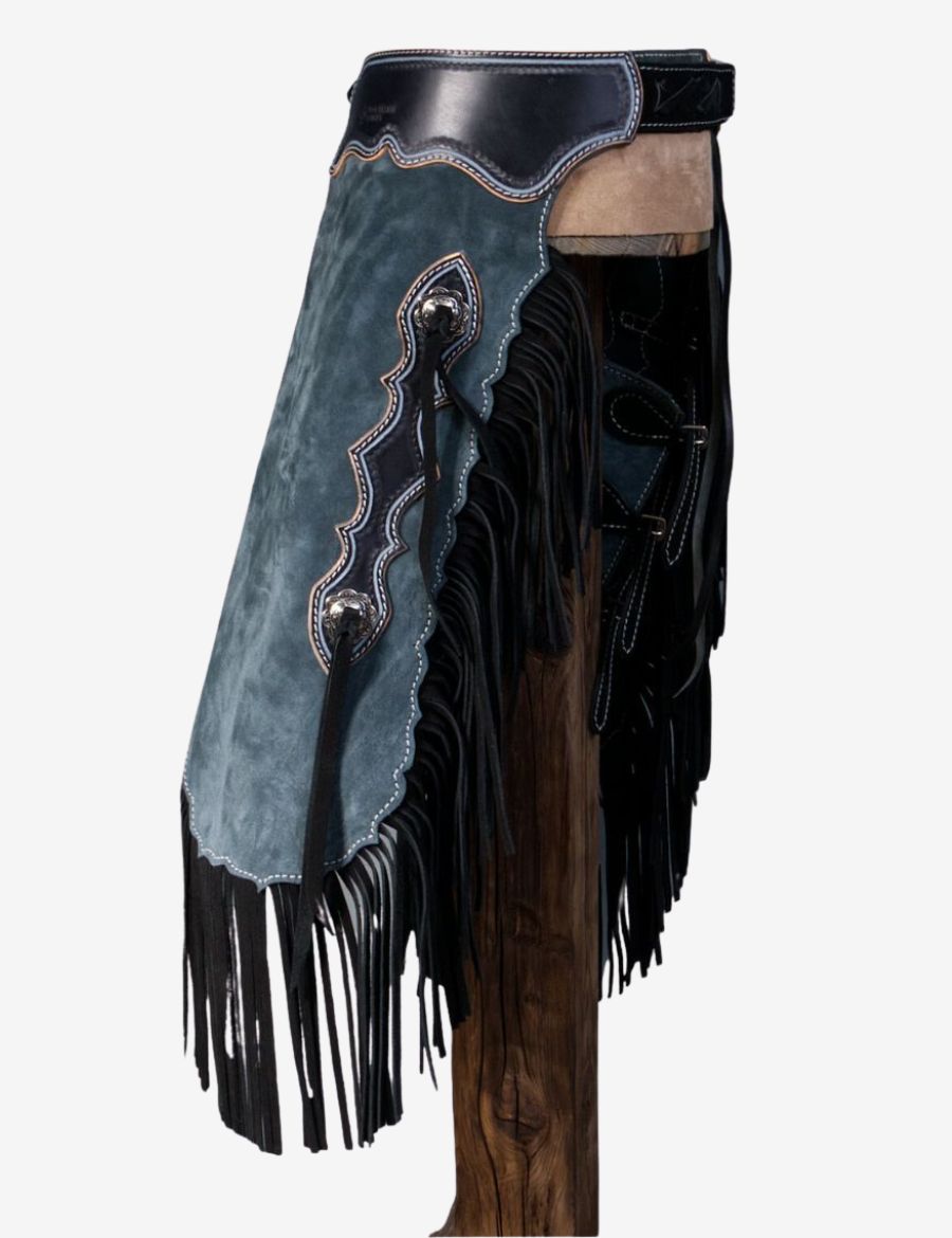 Close front detail of blue suede cowboy chinks chaps showing suede texture, black fringe, and stitched trim.
