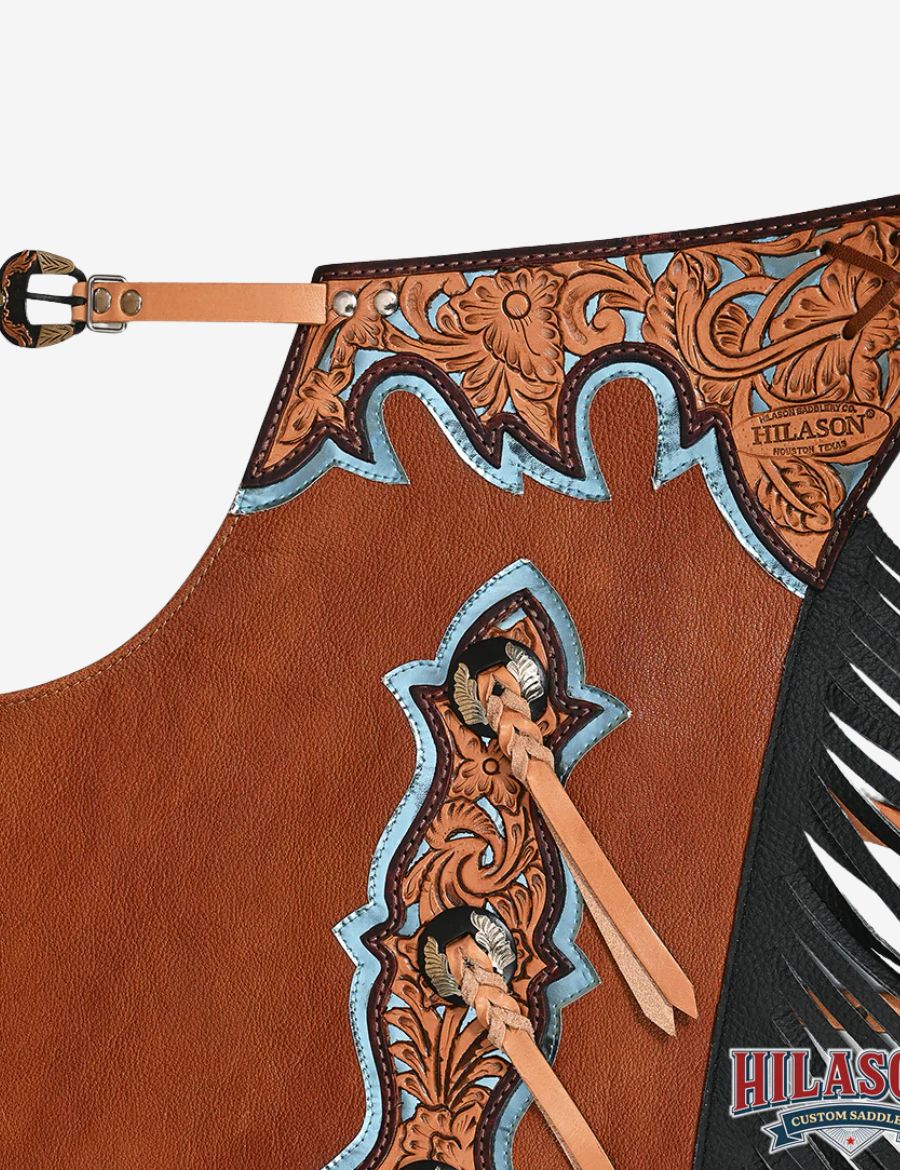 Close-up of floral tooled leather yoke on brown bull riding chaps with western carving and blue trim details.