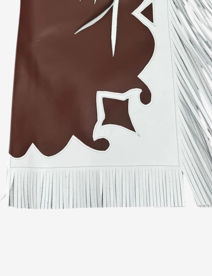 Lower leg detail of brown and white bull riding chaps with leather fringe and decorative western trim styling.