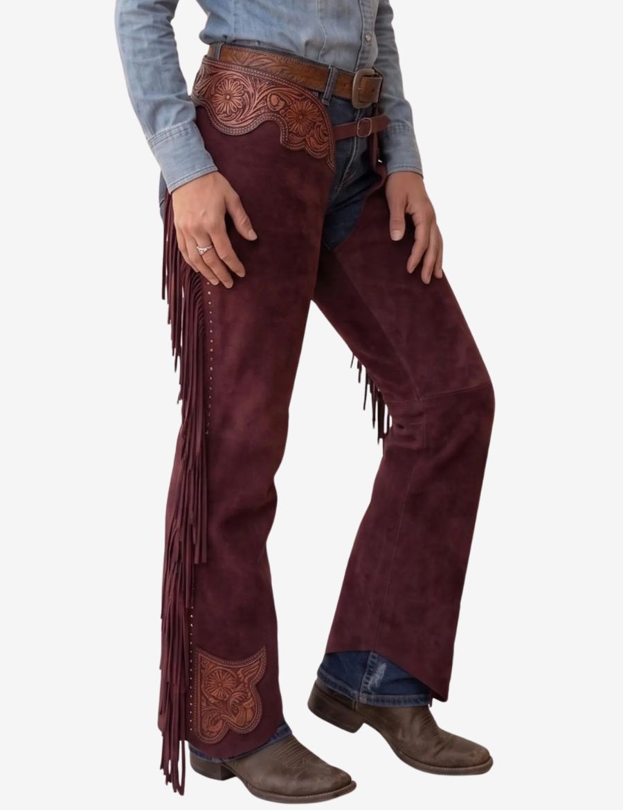Angled front view of burgundy suede western chaps with carved leather accents and flowing side fringe.