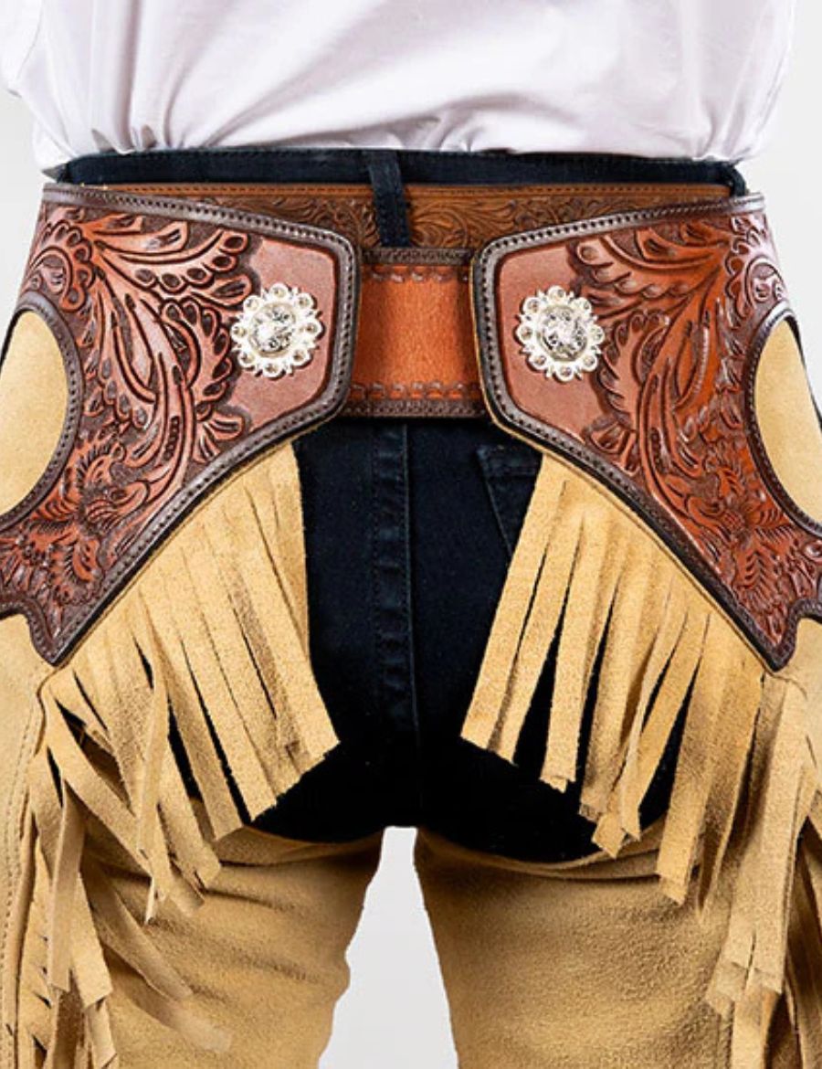 Rear close-up view of beige western chaps highlighting carved leather panels and layered suede fringe styling.