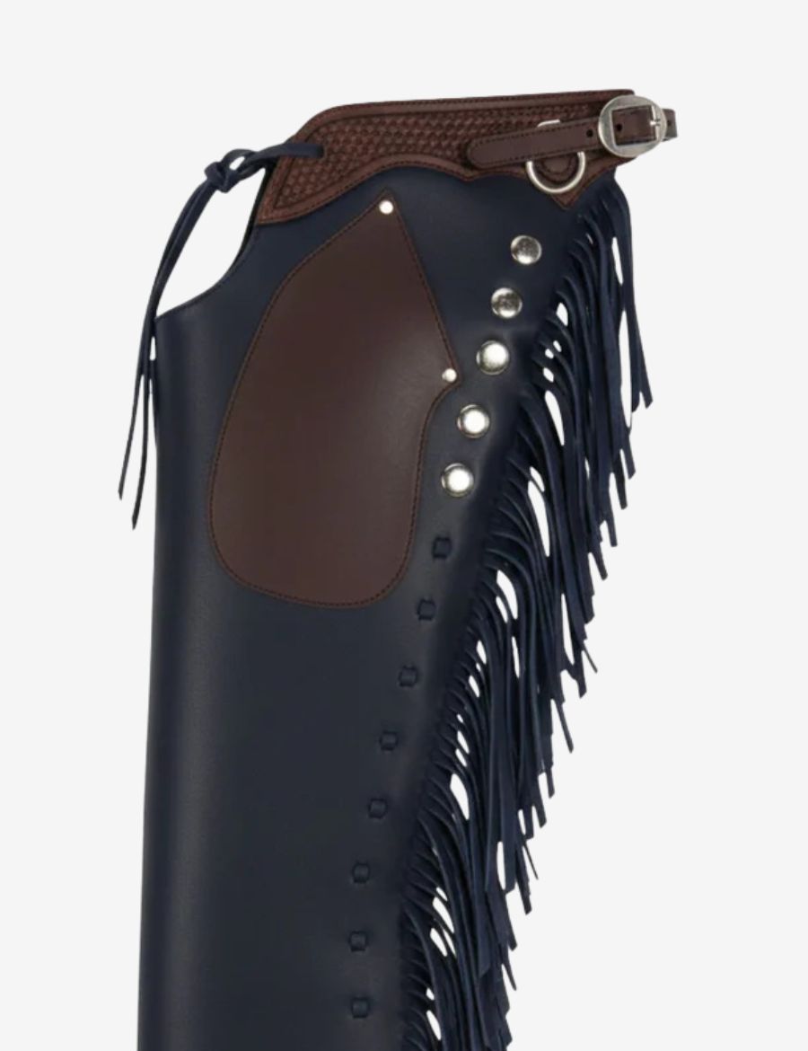 Close-up of deep navy leather shotgun chaps with brown knee patch, basketweave yoke, and silver conchos.