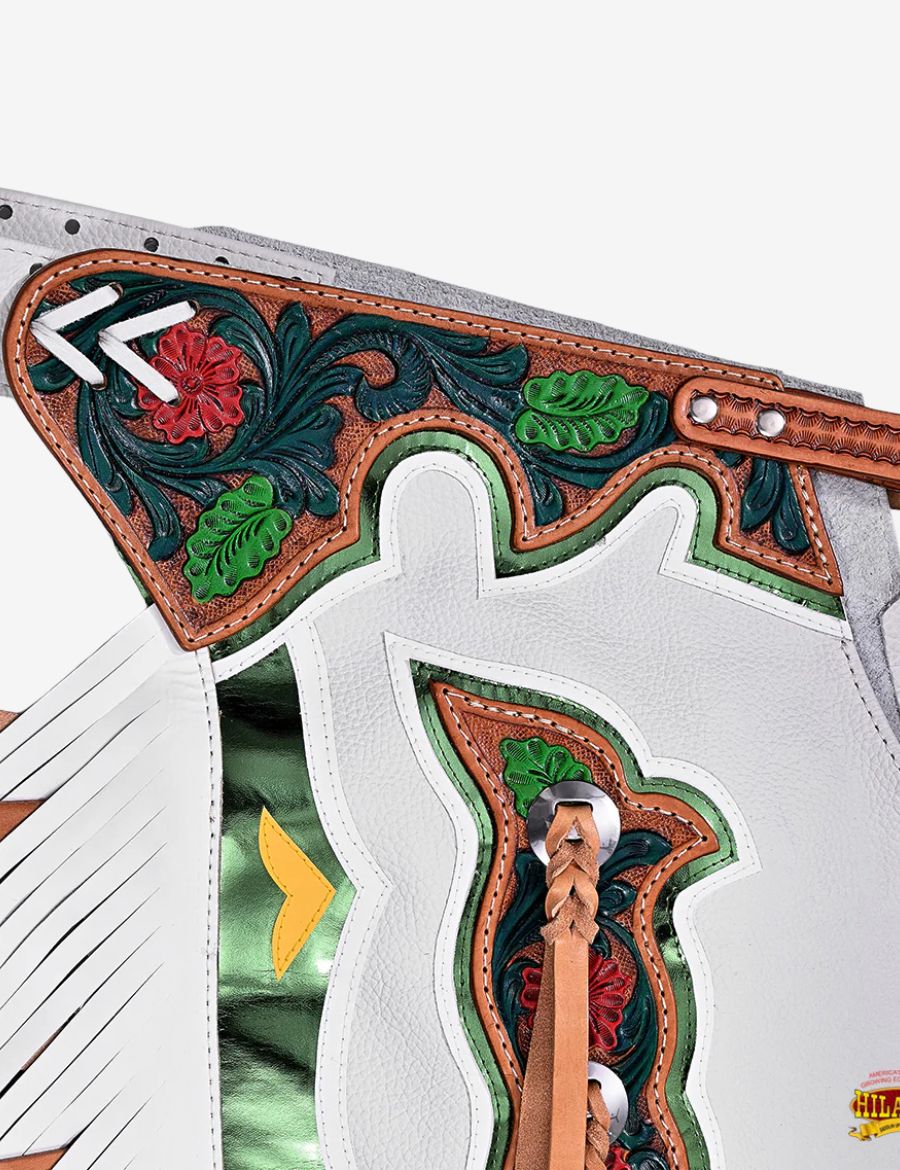Close-up floral tooling yoke detail on white rodeo chaps with green metallic inlays and western carving.