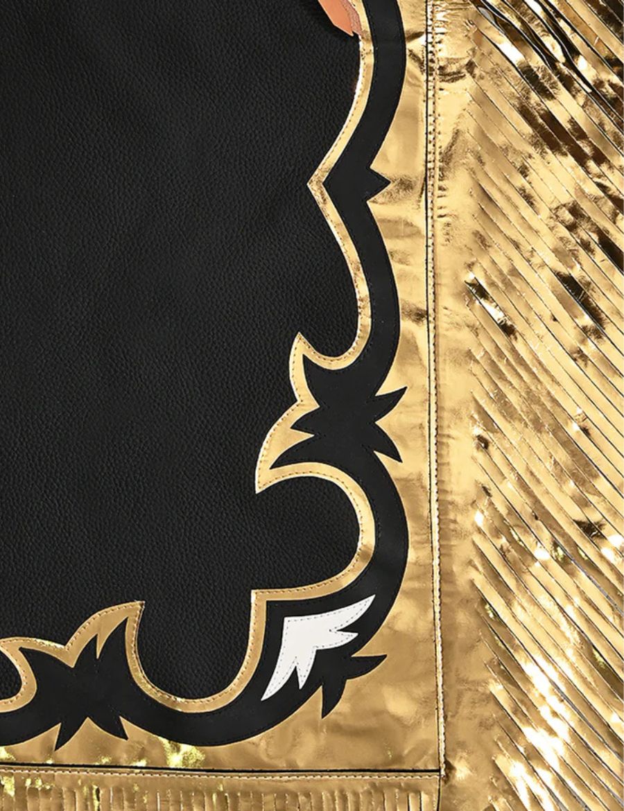 Lower leg close-up of black leather rodeo chaps featuring metallic gold trim, fringe, and western cut detailing.