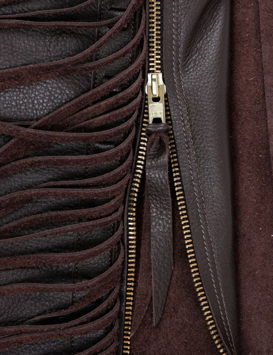 Close-up detail of heritage leather shotgun chaps featuring long fringe, zipper closure, and textured leather grain.