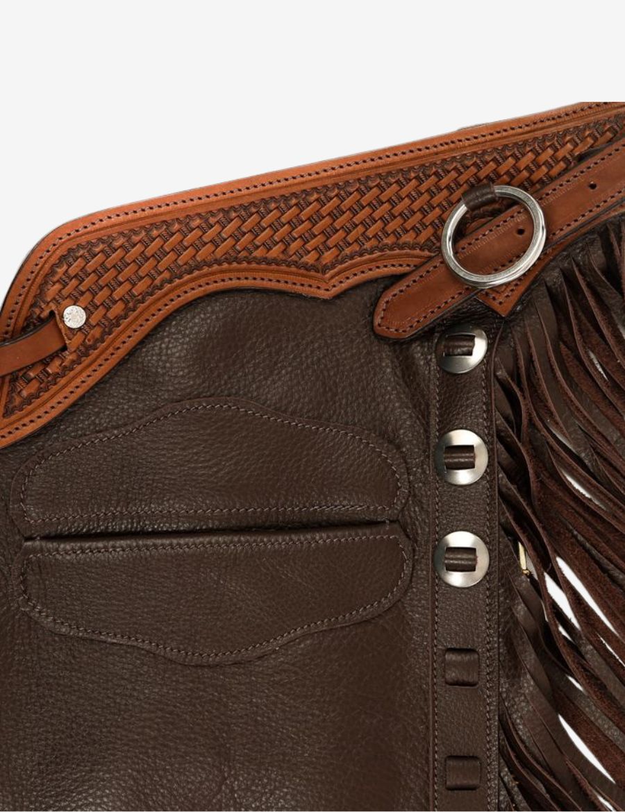 Close-up of heritage leather shotgun chaps showing basketweave tooling, fringe, and premium brown leather.