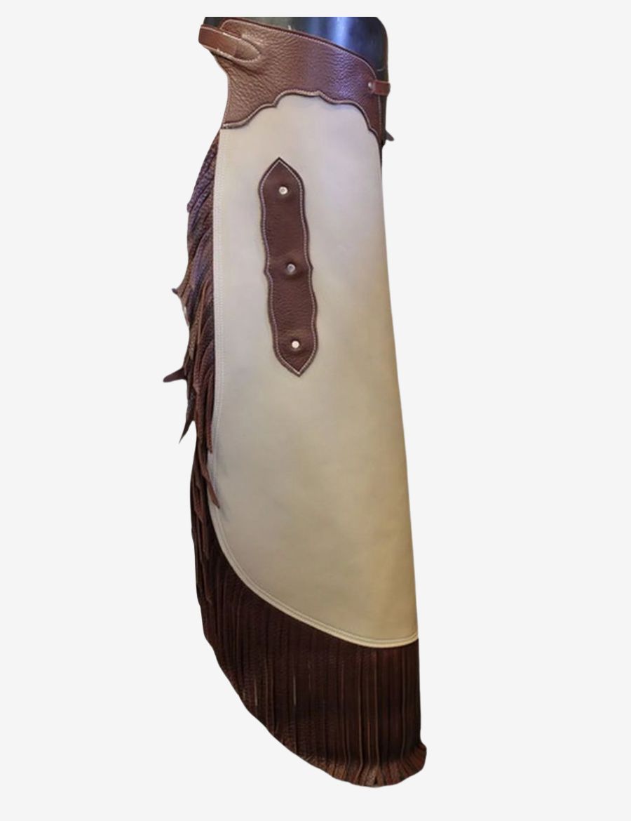Angled view of ivory leather cowboy chinks chaps featuring dark brown fringe, curved panels, and ranch craftsmanship.