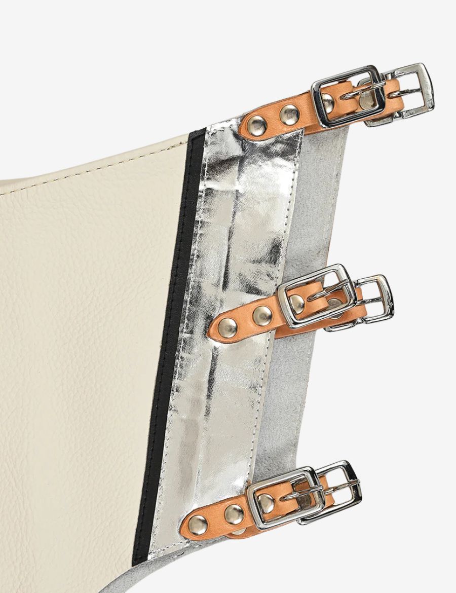 Leg closure detail of ivory rodeo chaps with silver metallic trim and adjustable buckle straps.