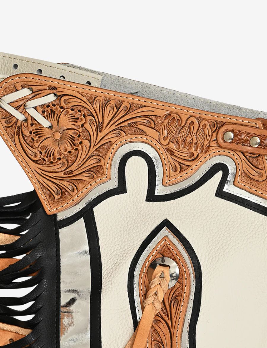 Close-up tooling detail of ivory rodeo chaps with floral carved leather and black accent trim.