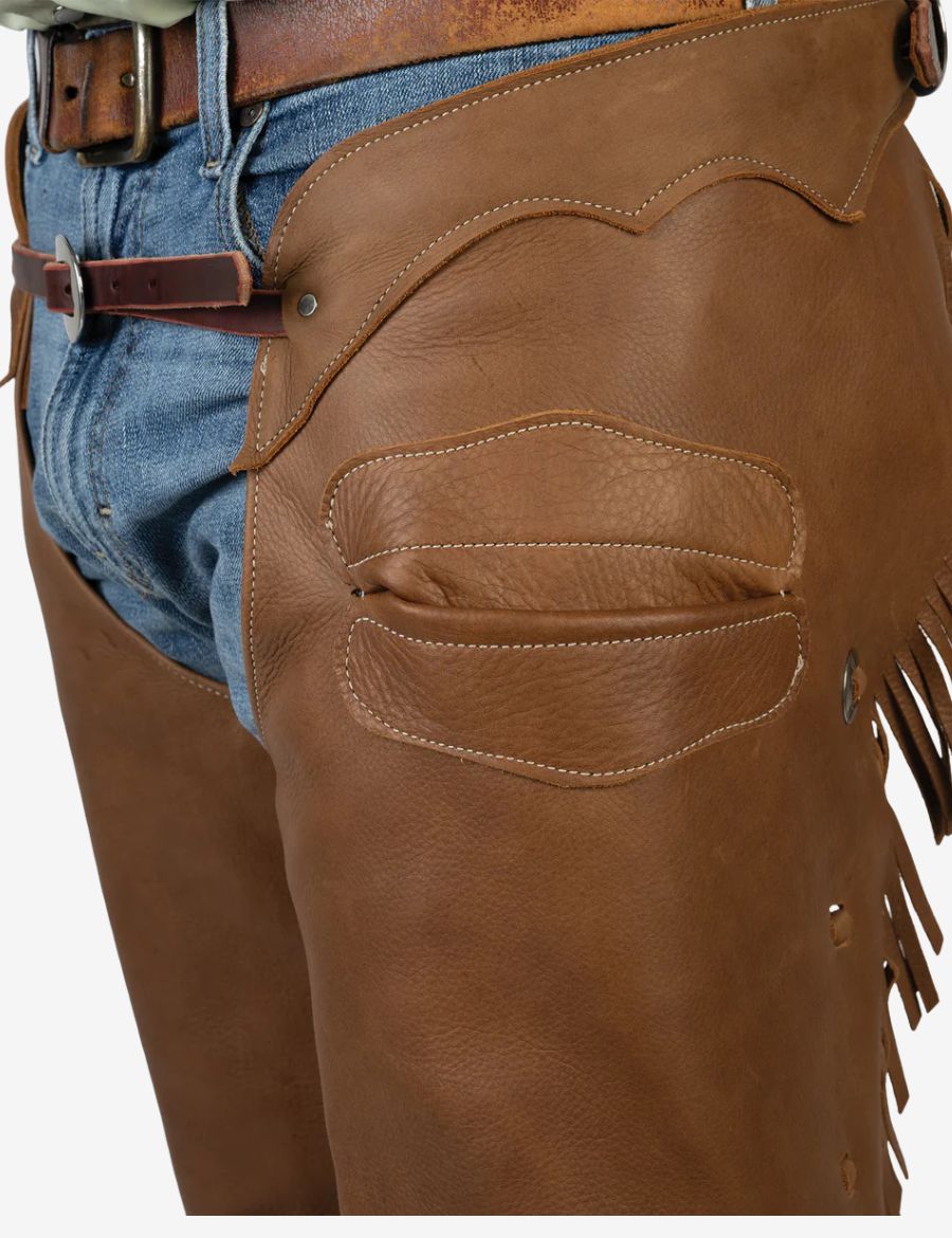 Close-up of mens saddle brown leather western chaps highlighting textured leather and reinforced western panels.
