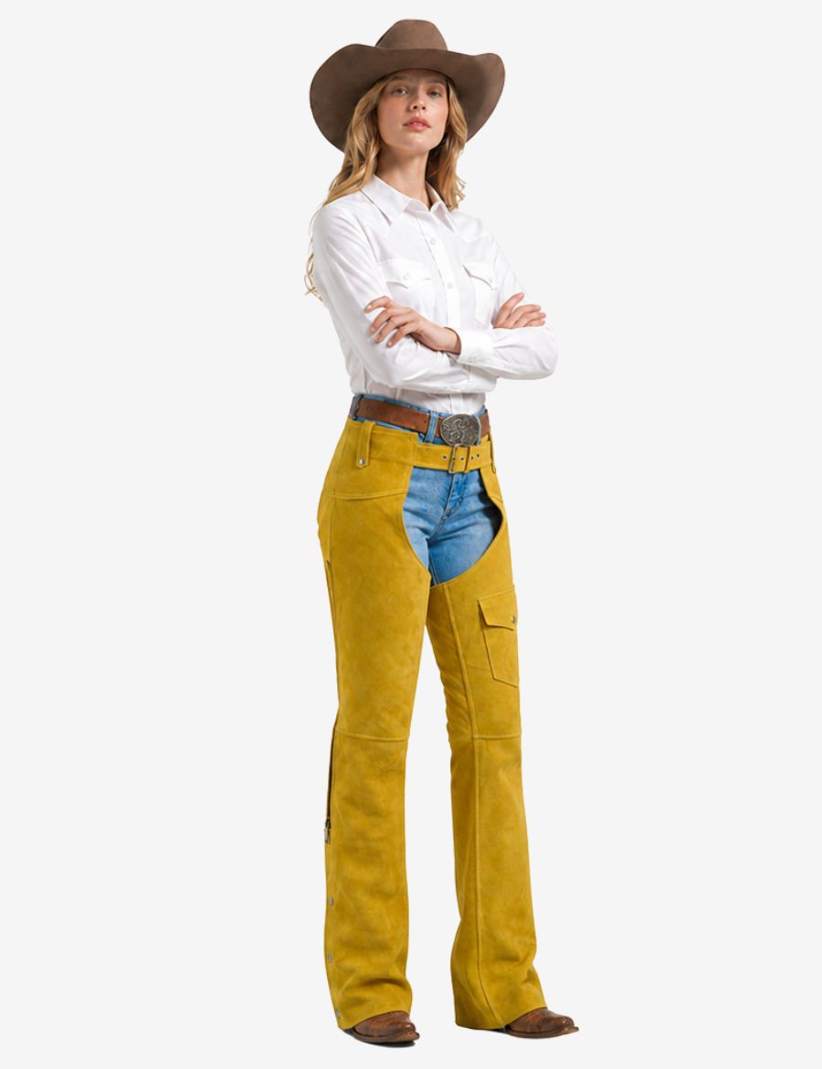 Women wearing mustard western chaps with fringe paired with denim jeans, cowboy boots, and western shirt.