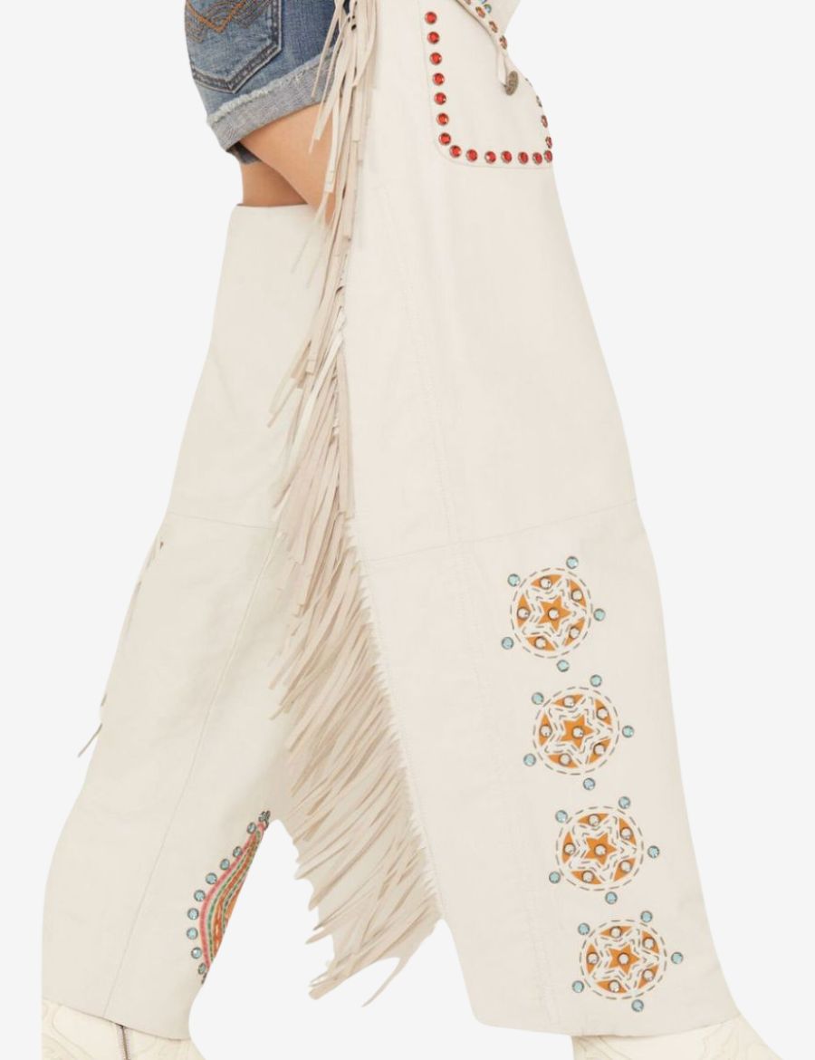 Side detail view of white cowgirl chaps featuring long fringe accents and decorative western artwork patterns.