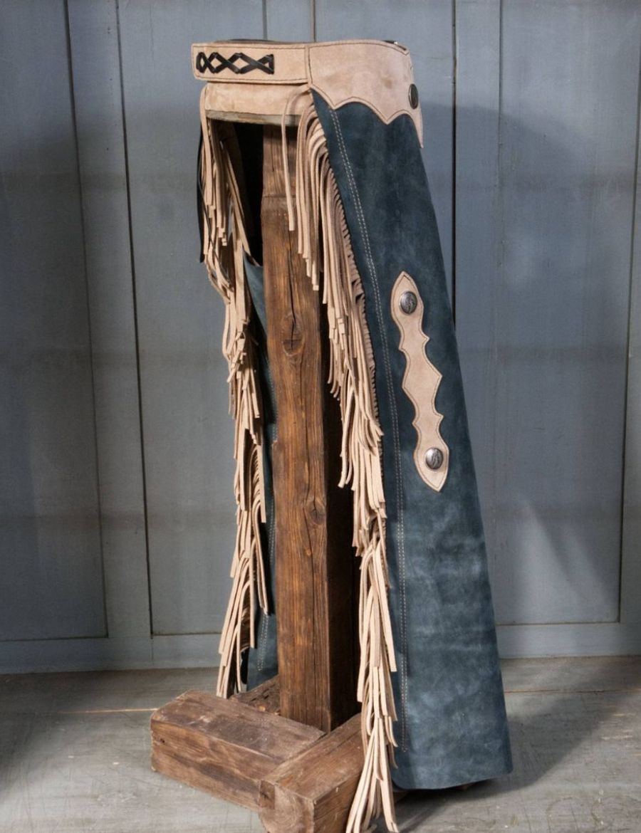 Angled back view of vintage blue suede fringe cowboy chaps with beige leather trim and fringe details.