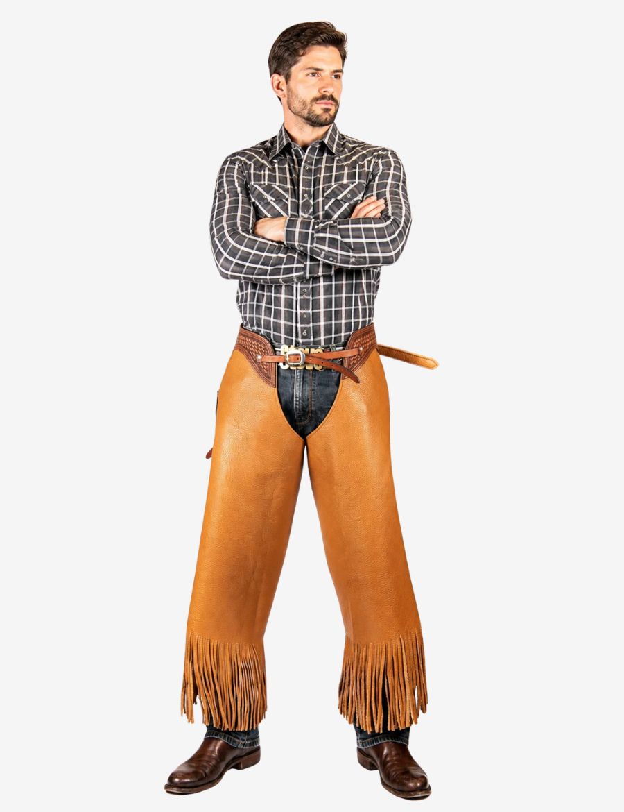 Western cognac cowhide chinks chaps styled on cowboy model with premium leather finish, fringe trim, and authentic ranch-ready look.