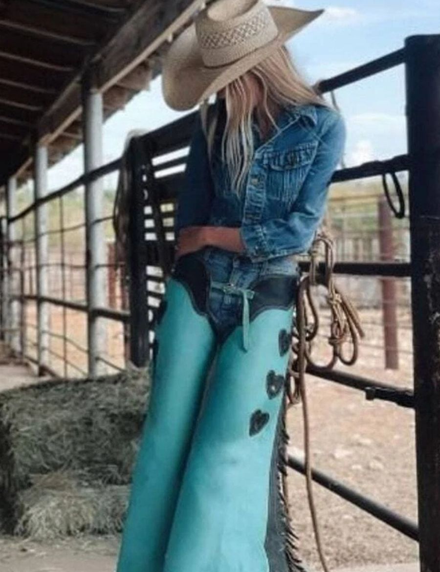 Female model wearing turquoise western cowgirl chaps with black leather trim and fringe side accents.