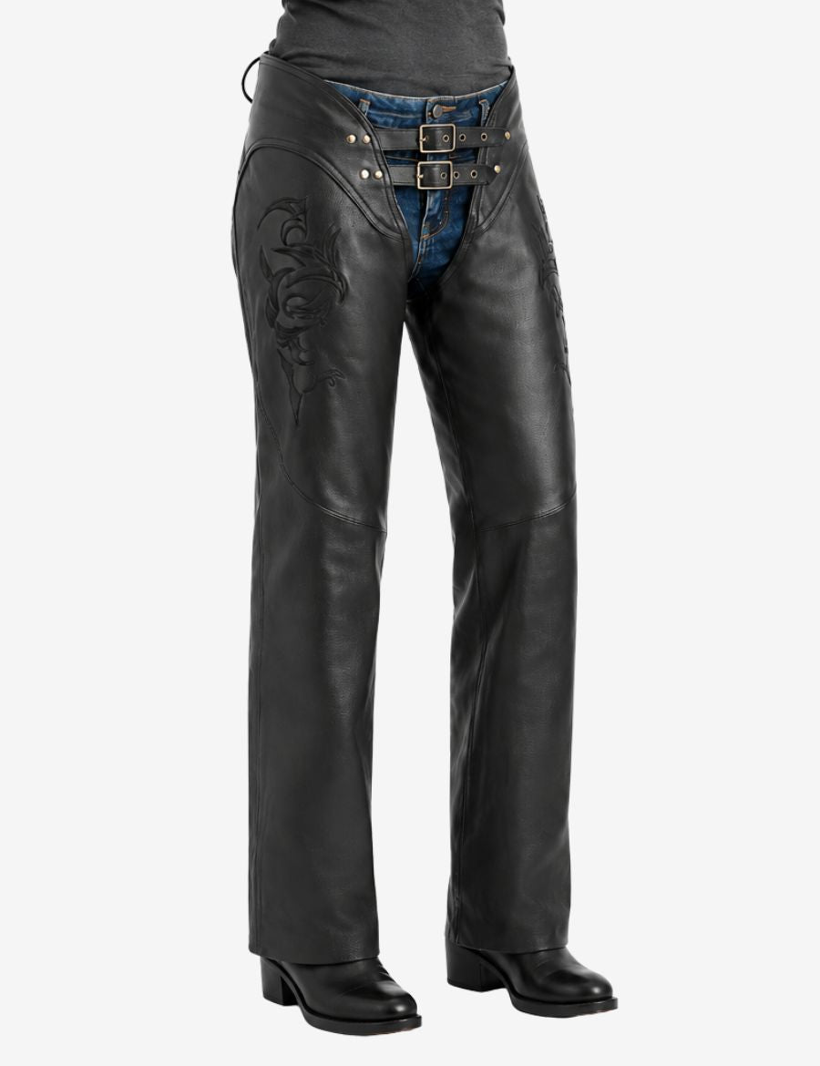 Front view of womens floral embroidered biker chaps featuring black leather construction, subtle floral embossing, double-buckle waist straps, and motorcycle riding fit over denim jeans.
